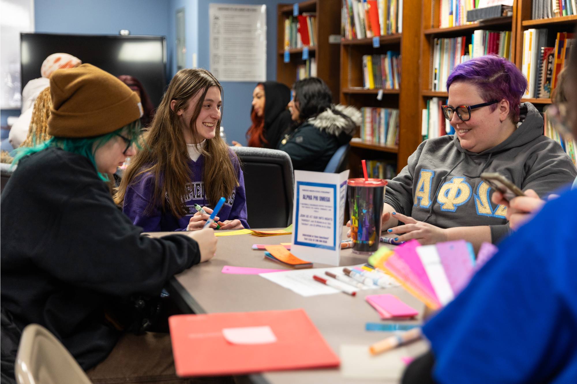 Students sitting at a table, smiling, and working on craft projects with colored paper